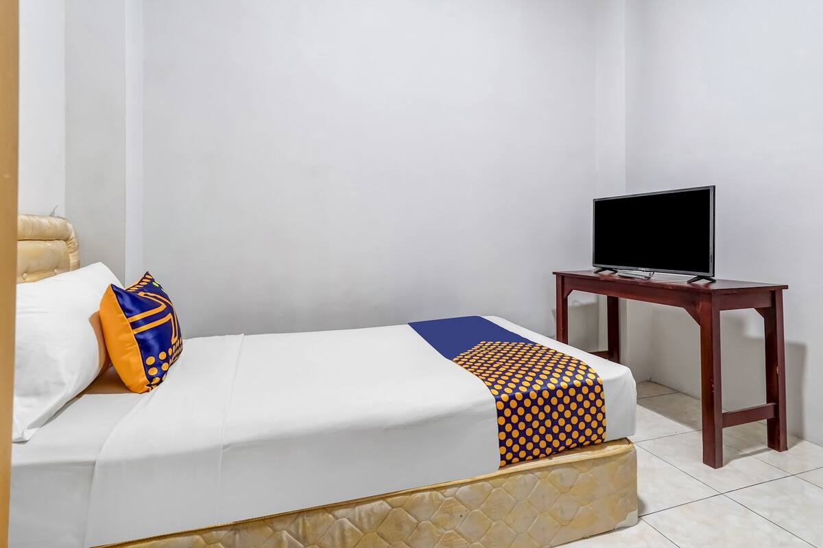 Habitació d'hotel amb un llit, una televisió sobre una taula de fusta i un llençol estampat.