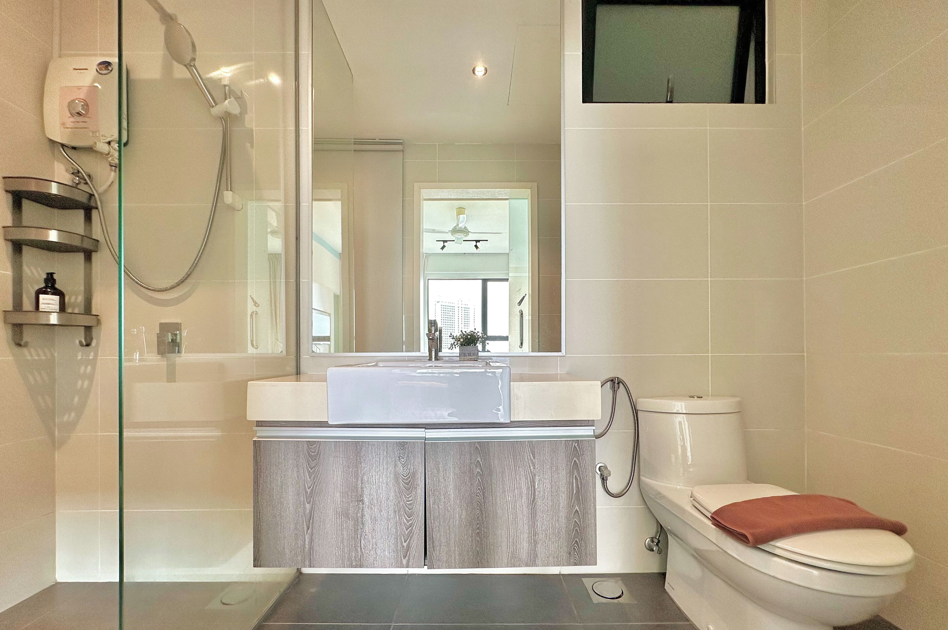 Un bany modern amb un envà de dutxa de vidre, un lavabo blanc sobre un moble de tocador de fusta i un vàter blanc.