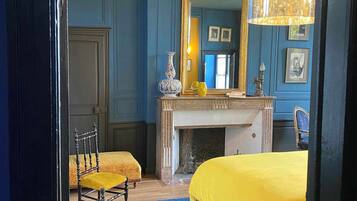 A bedroom with two beds, a chair, a fireplace, and a mirror.