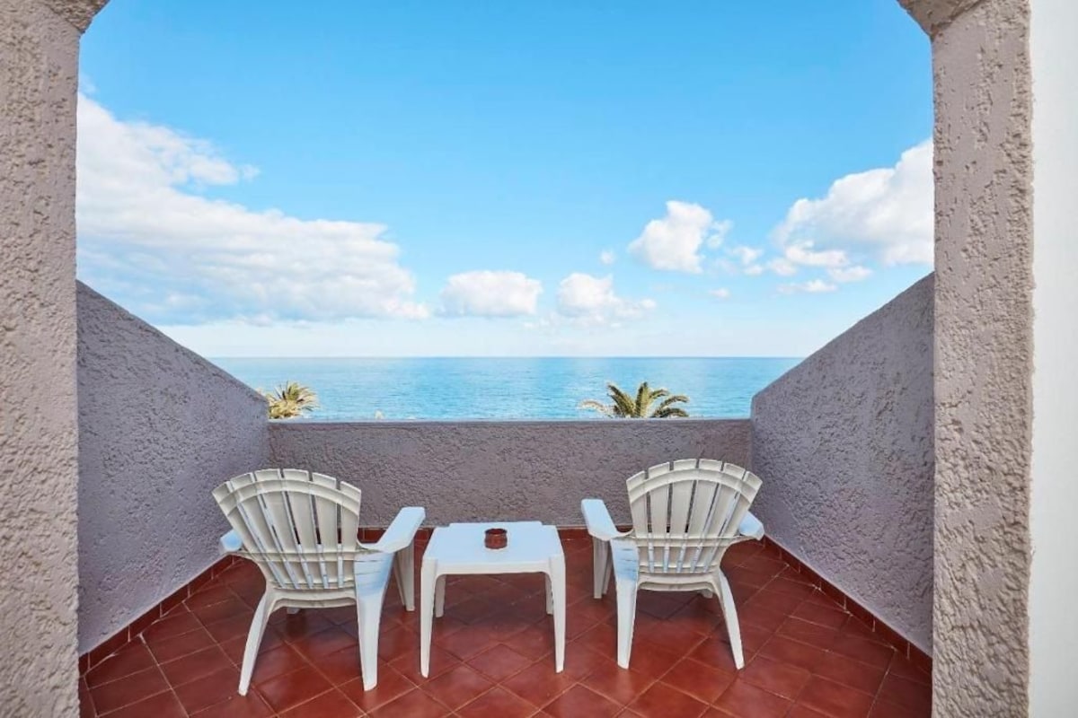 A balcony with two white chairs and a small table, overlooking a body of water.