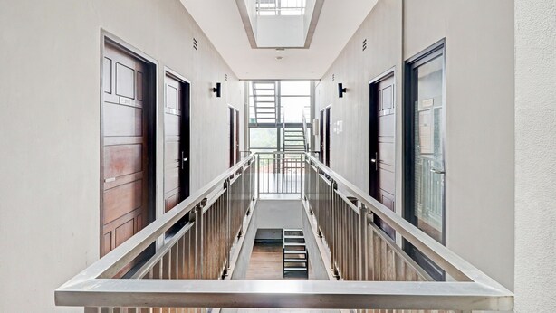 A modern hotel corridor with a central staircase, metal railings, and large doors on either side. - OYO 94732 D River Cihampelas (Bandung)