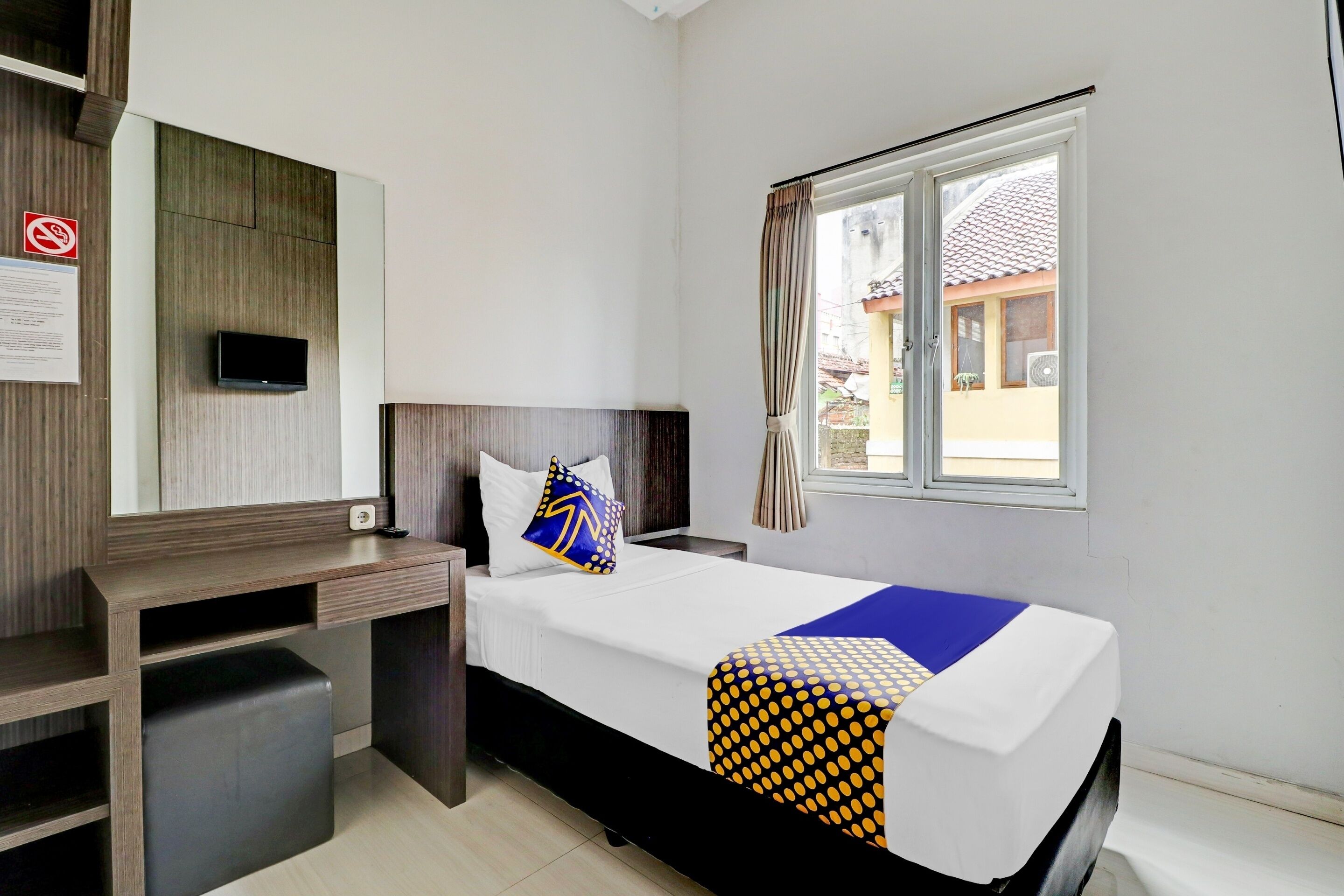 Une chambre d’hôtel avec un lit, un bureau, une télévision et une fenêtre avec des rideaux.