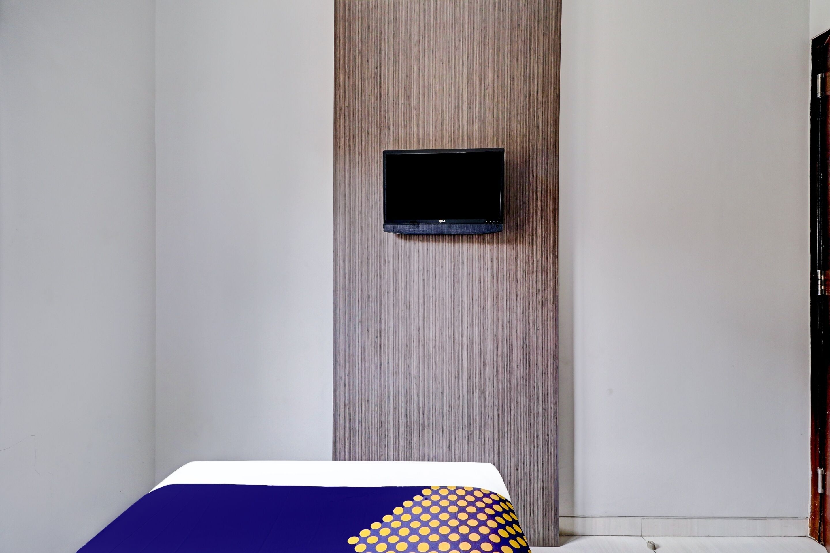 Una habitación de hotel con una cama, un televisor montado en un panel de madera y una pared blanca.