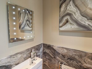A bathroom with a vanity, a mirror with lights, and marble walls. - Tidal Watch (Seahouses)