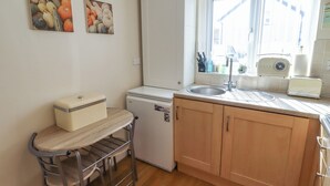 Eine kompakte Küche mit Kühlschrank, Spüle und Toaster. Ein kleiner Tisch mit Hocker und ein Fenster sorgen für natürliches Licht.