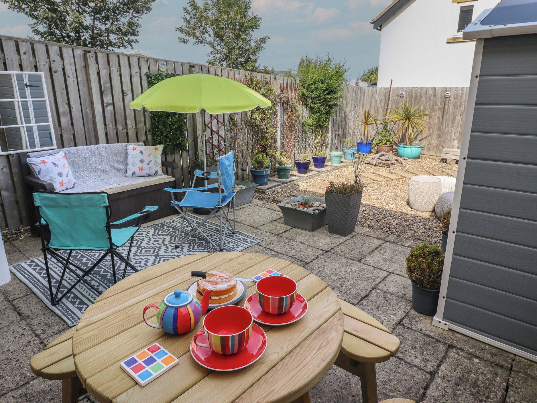 A patio with a table set for tea, a folding chair, and a small garden area with potted plants.