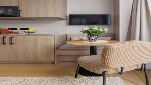 Een moderne keuken met een magnetron, een flatscreen televisie, een eethoek met een ronde tafel en een geweven stoel, en een bank met kussens.