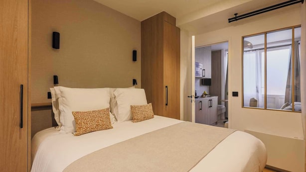 Een moderne hotelkamer met een groot bed, een kledingkast, een bureau en een raam met gordijnen.