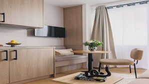 Een moderne woonkamer met een bank, een bijzettafeltje met boeken, een aan de muur bevestigde televisie en een raam met gordijnen.