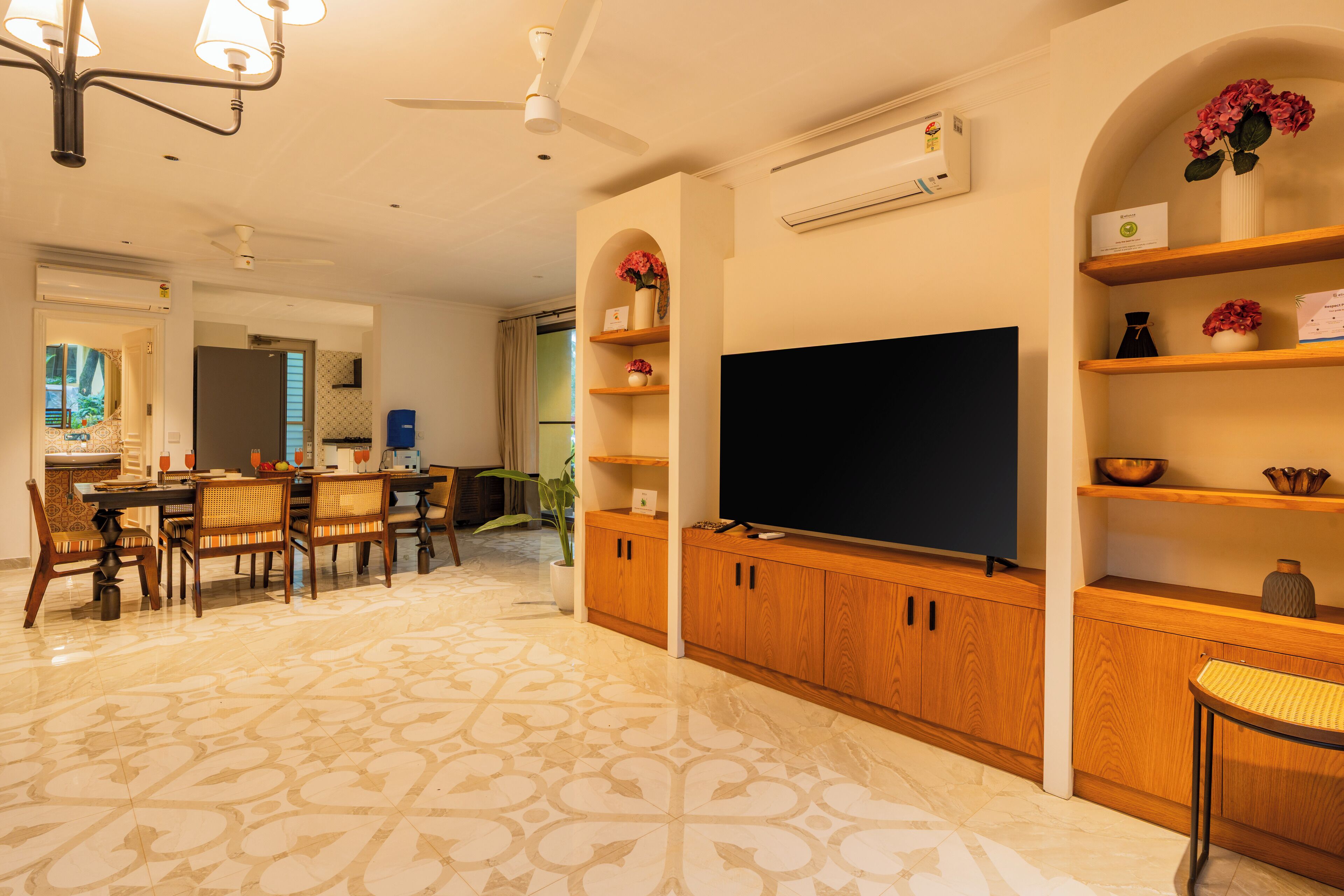 A spacious living room with a large flat-screen TV, wooden cabinets, and a patterned floor.
