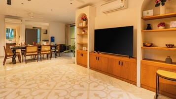 A spacious living room with a large flat-screen TV, wooden cabinets, and a patterned floor.