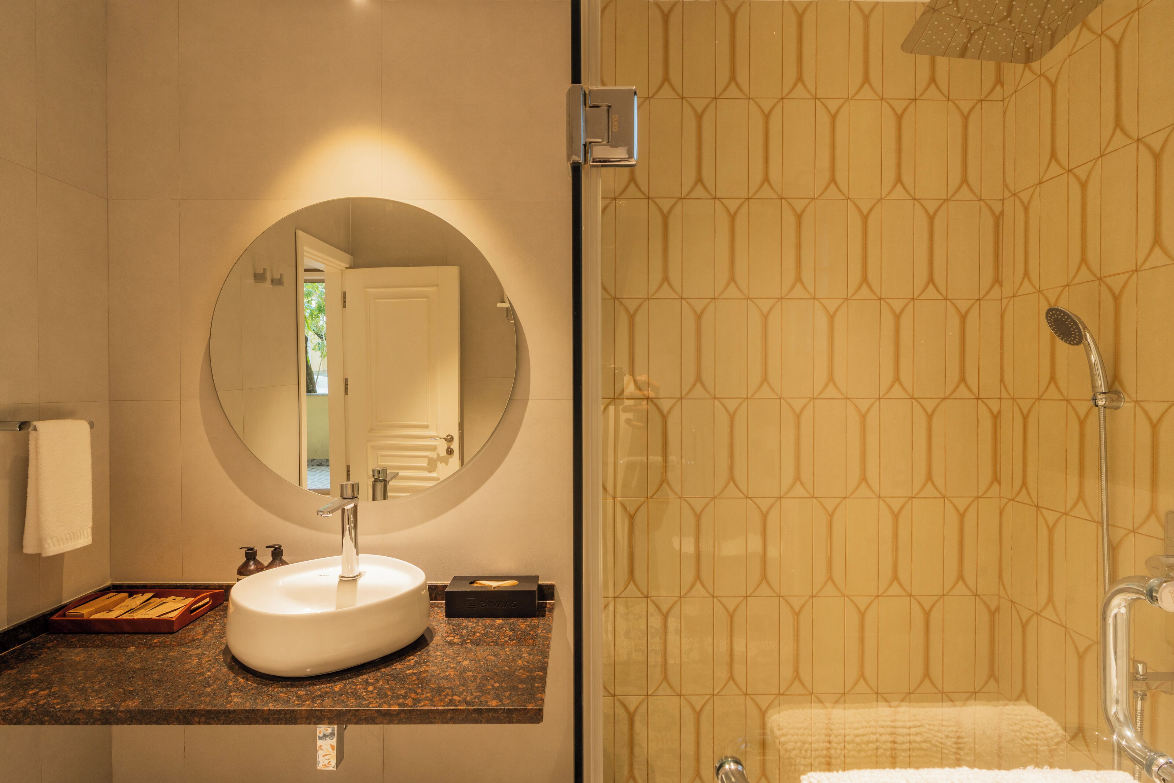 A bathroom with a round mirror, a sink, a shower, and a towel rack.