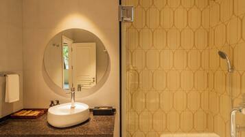 A bathroom with a round mirror, a sink, a shower, and a towel rack.