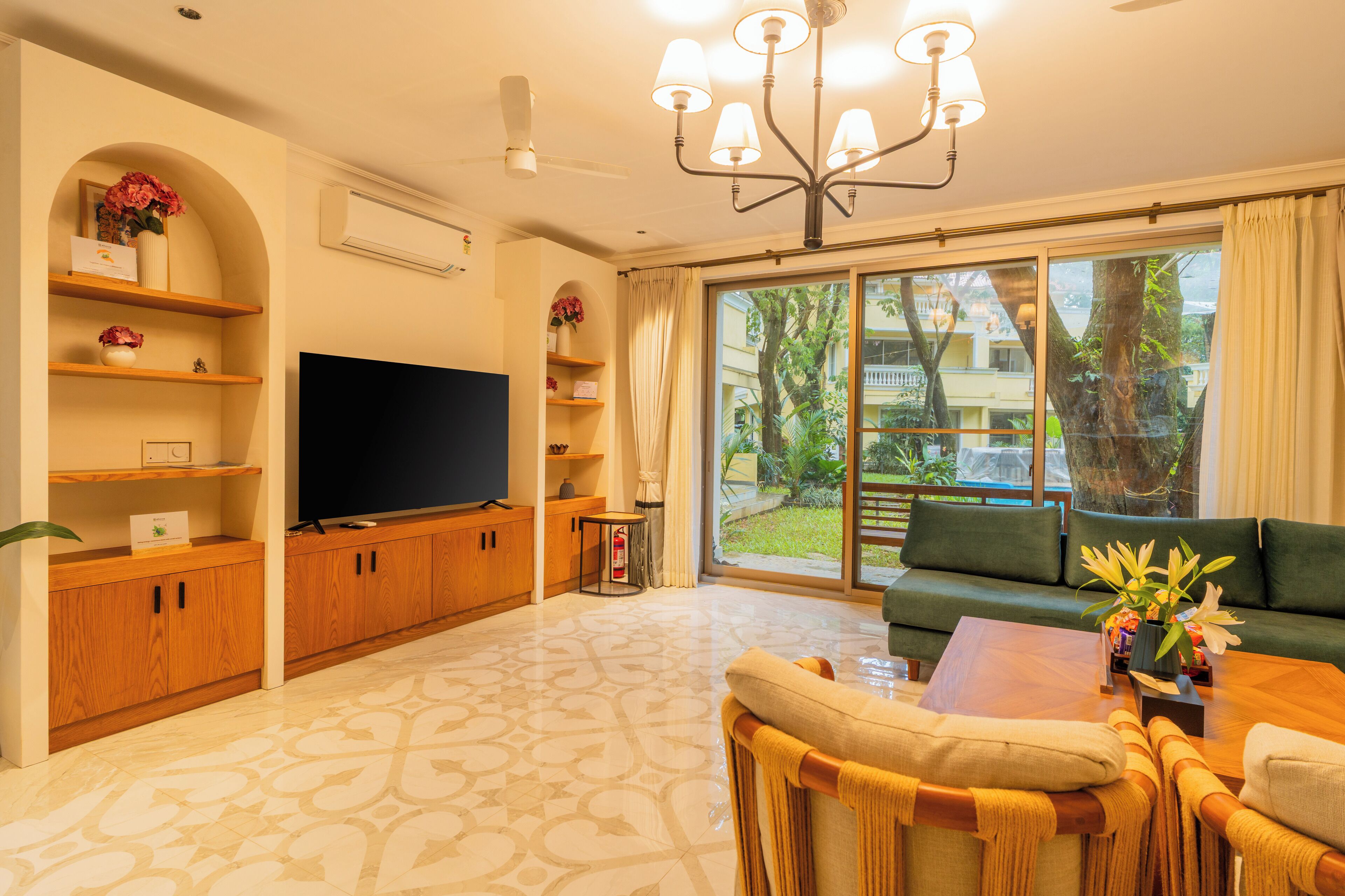 A living room with a flat-screen TV, wooden cabinets, a sofa, a coffee table, and a large window with a view of greenery and buildings.
