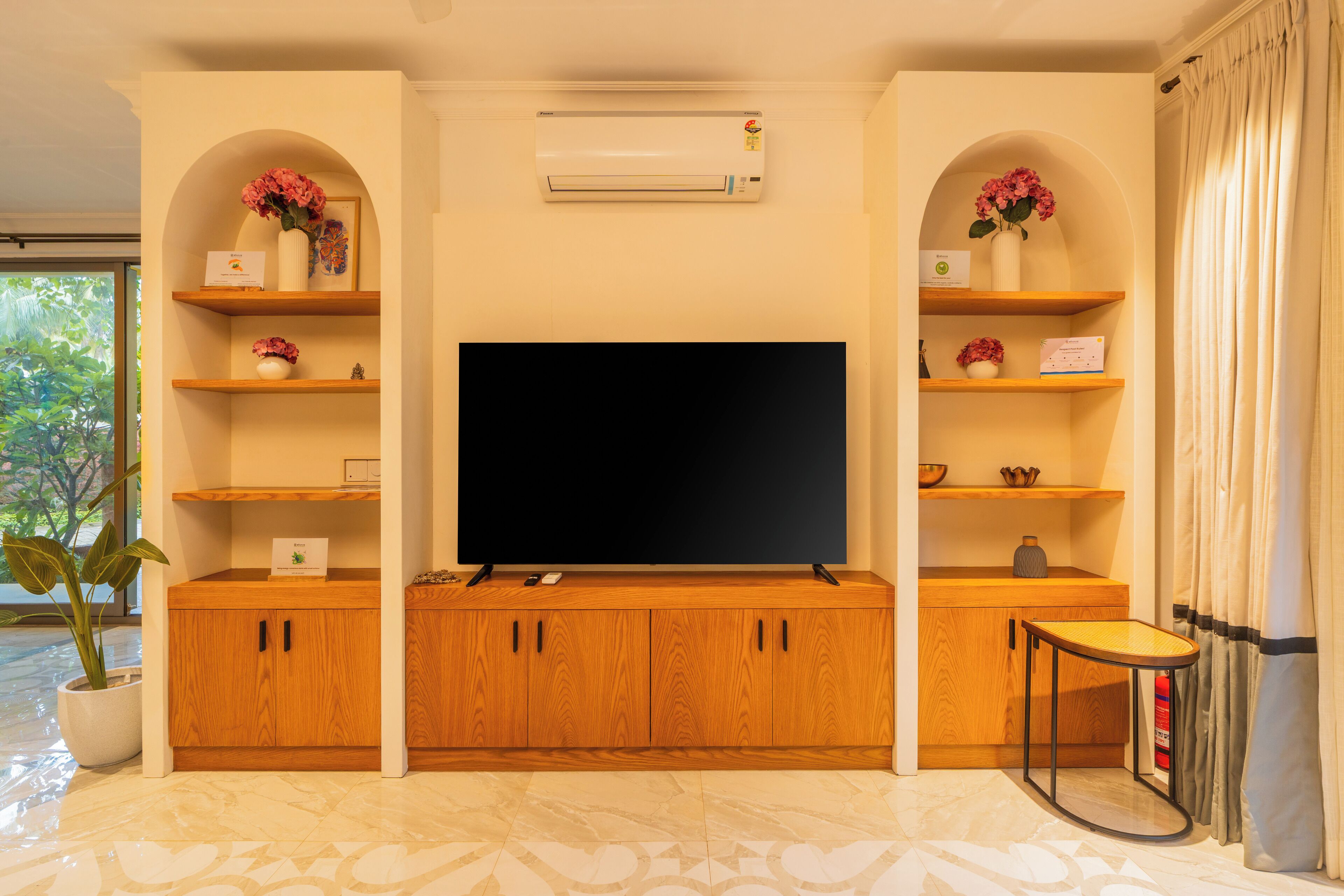 A living room with a flat-screen TV, wooden cabinets, and shelves with decorative items.