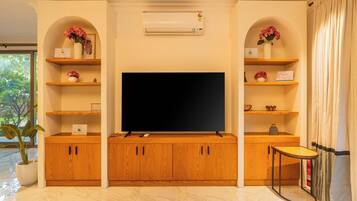 A living room with a flat-screen TV, wooden cabinets, and shelves with decorative items.