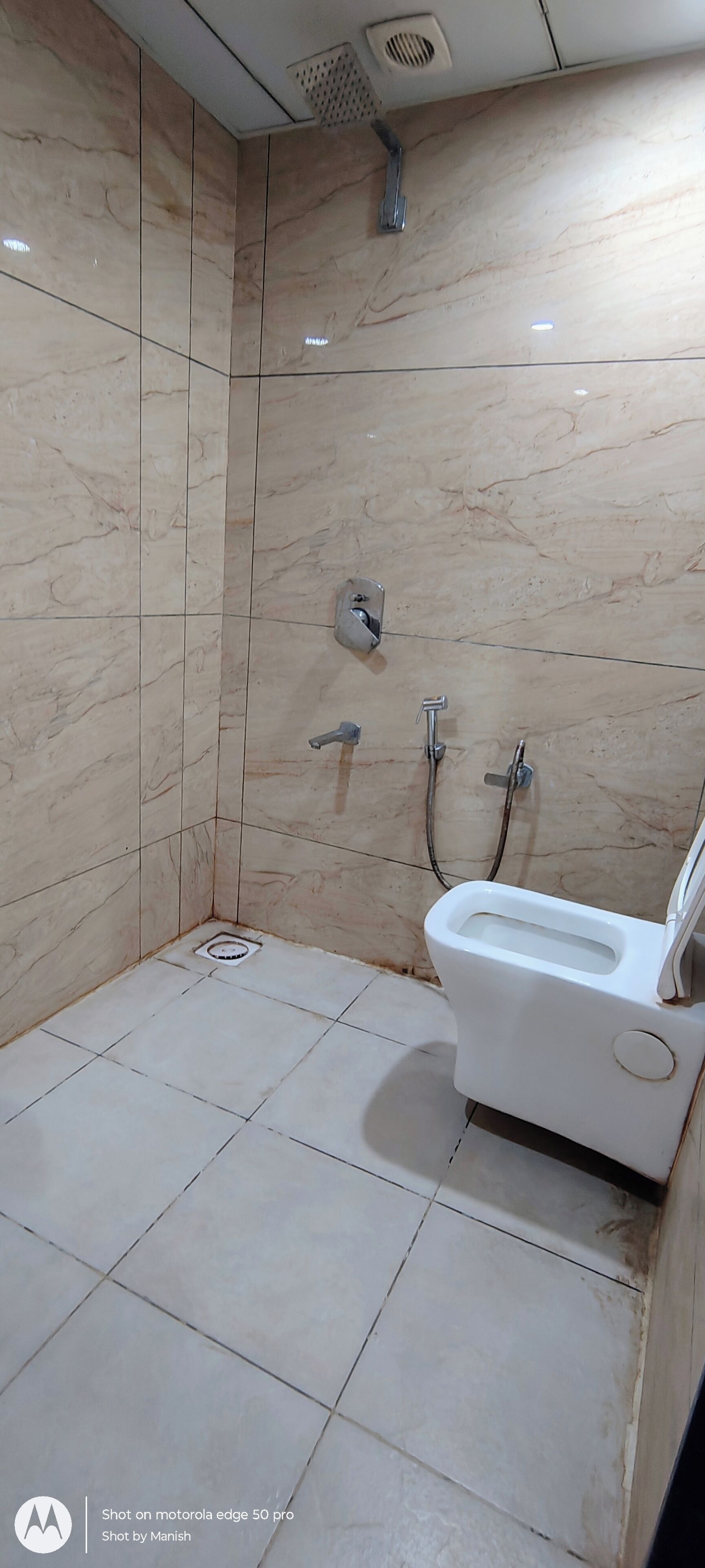 Un baño con inodoro blanco, ducha y lavamanos. Las paredes están cubiertas de un diseño que imita el mármol.