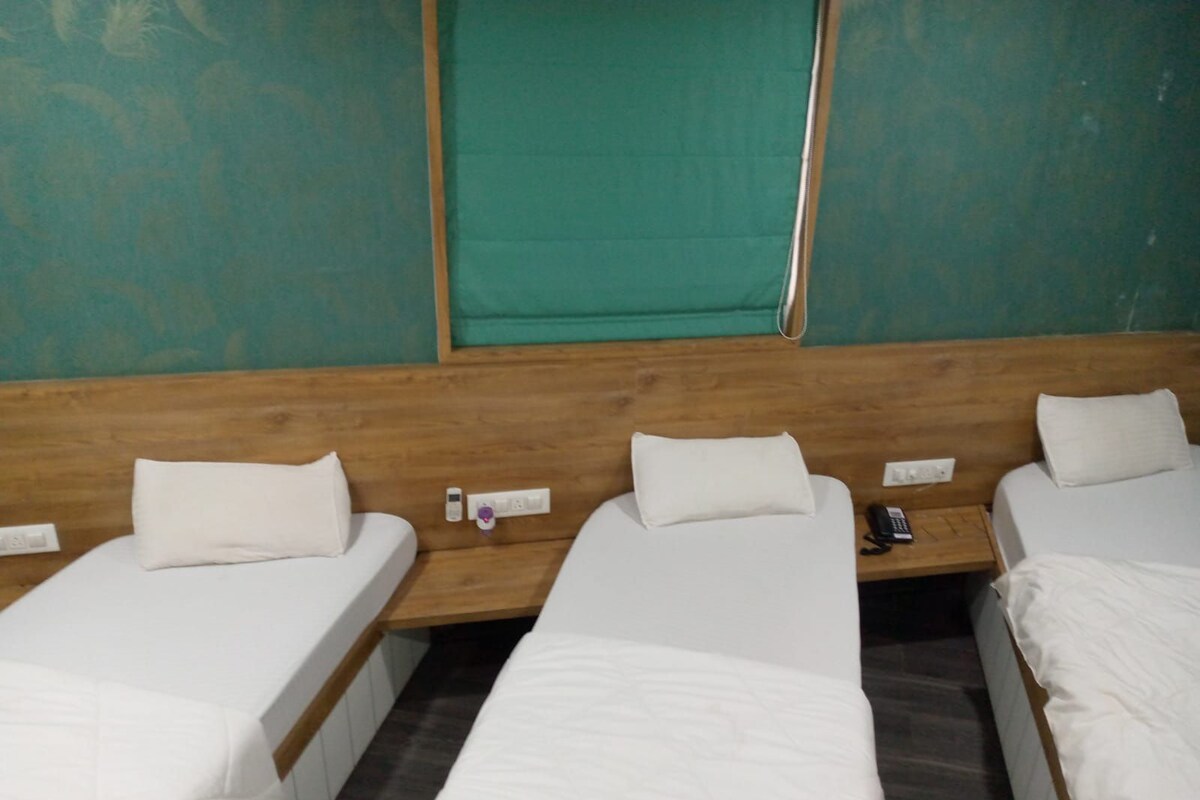 A hotel room with three single beds, wooden headboards, and a green wall.