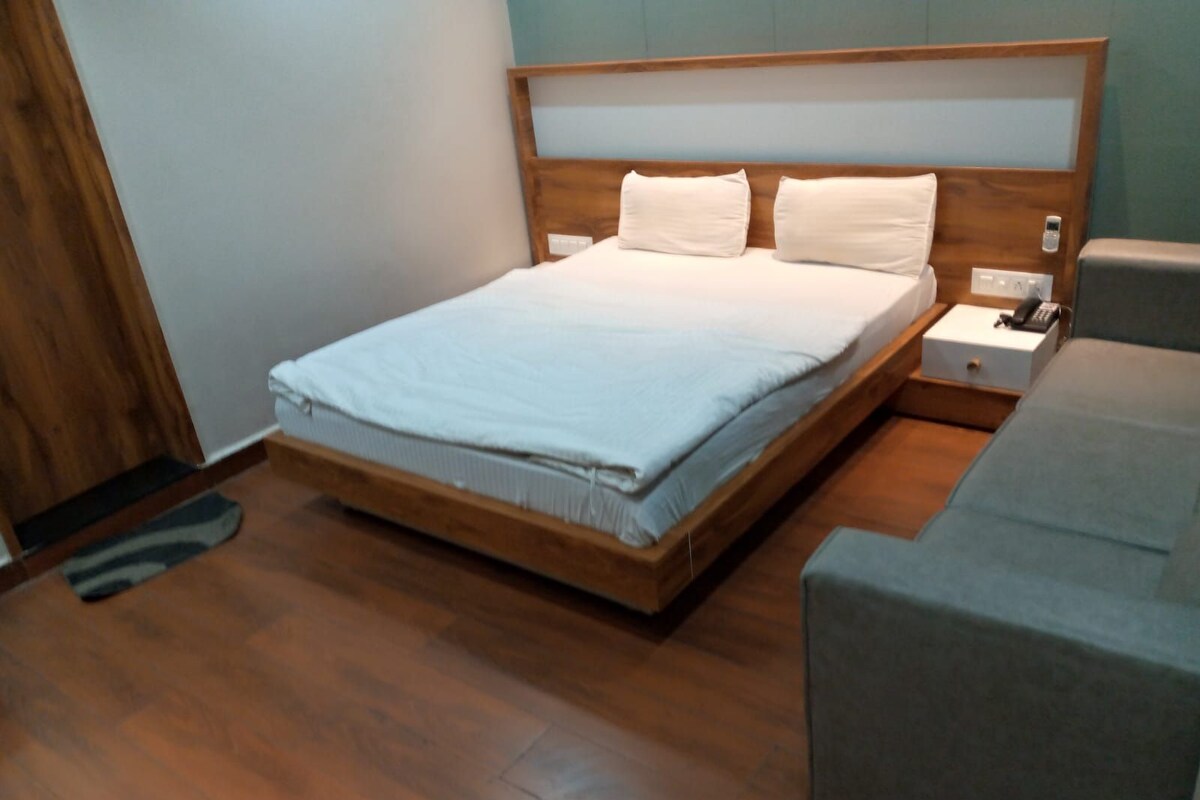 A modern bedroom with a wooden bed frame, a grey sofa, and a bedside table with a phone and a box.