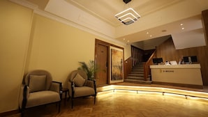 Un espace d’accueil comprenant un comptoir de réception en bois, deux chaises, un escalier et un sol décoré d’un motif en chevrons.