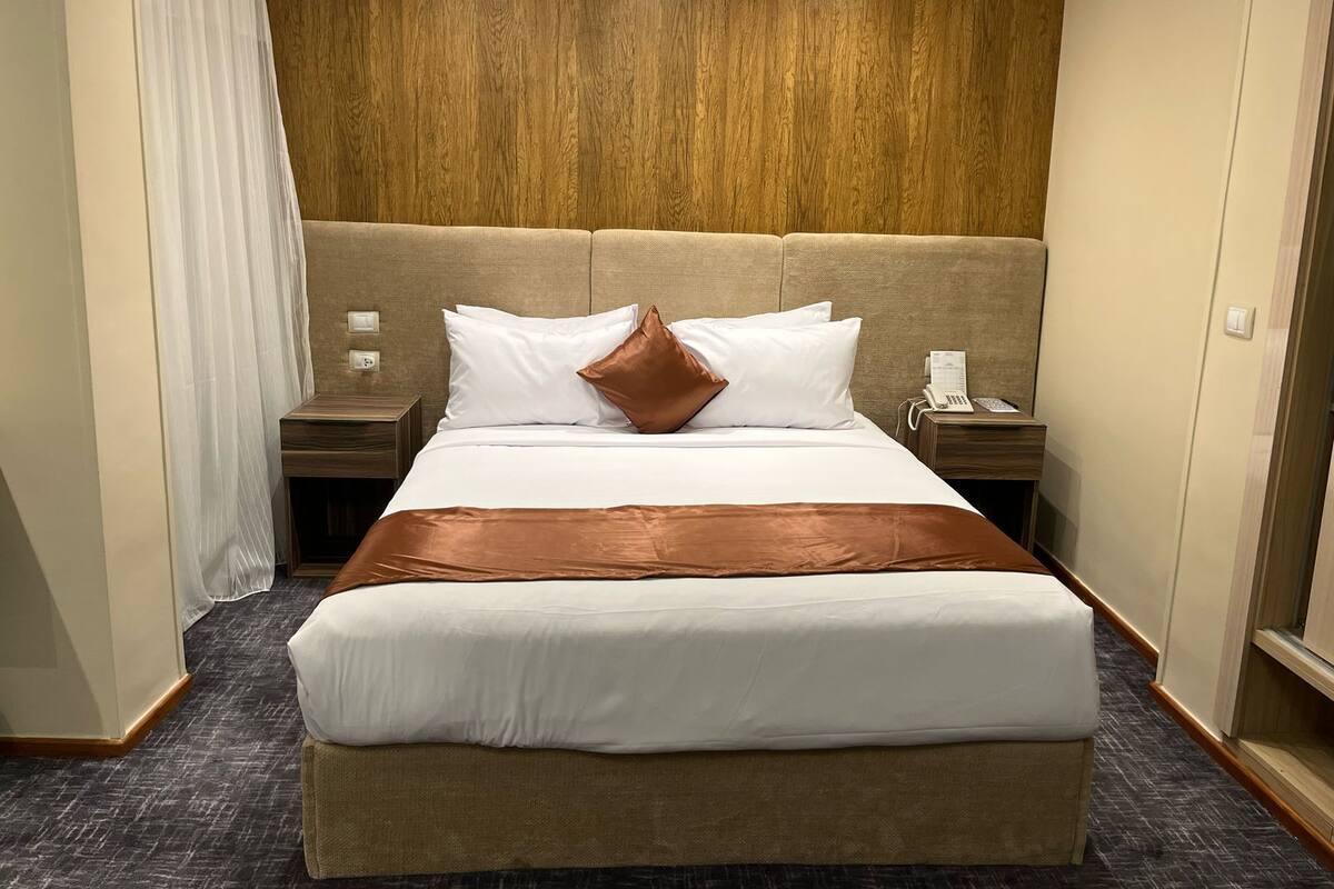 A hotel room with a large bed, a wooden headboard, a telephone, and a nightstand.