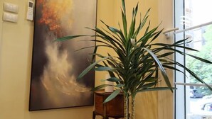 Un couloir avec une plante en pot, un tableau accroché au mur et une fenêtre donnant sur l’extérieur.