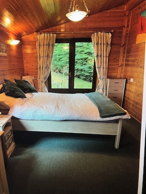 A wooden cabin bedroom with a bed, curtains, a desk, and a dresser.