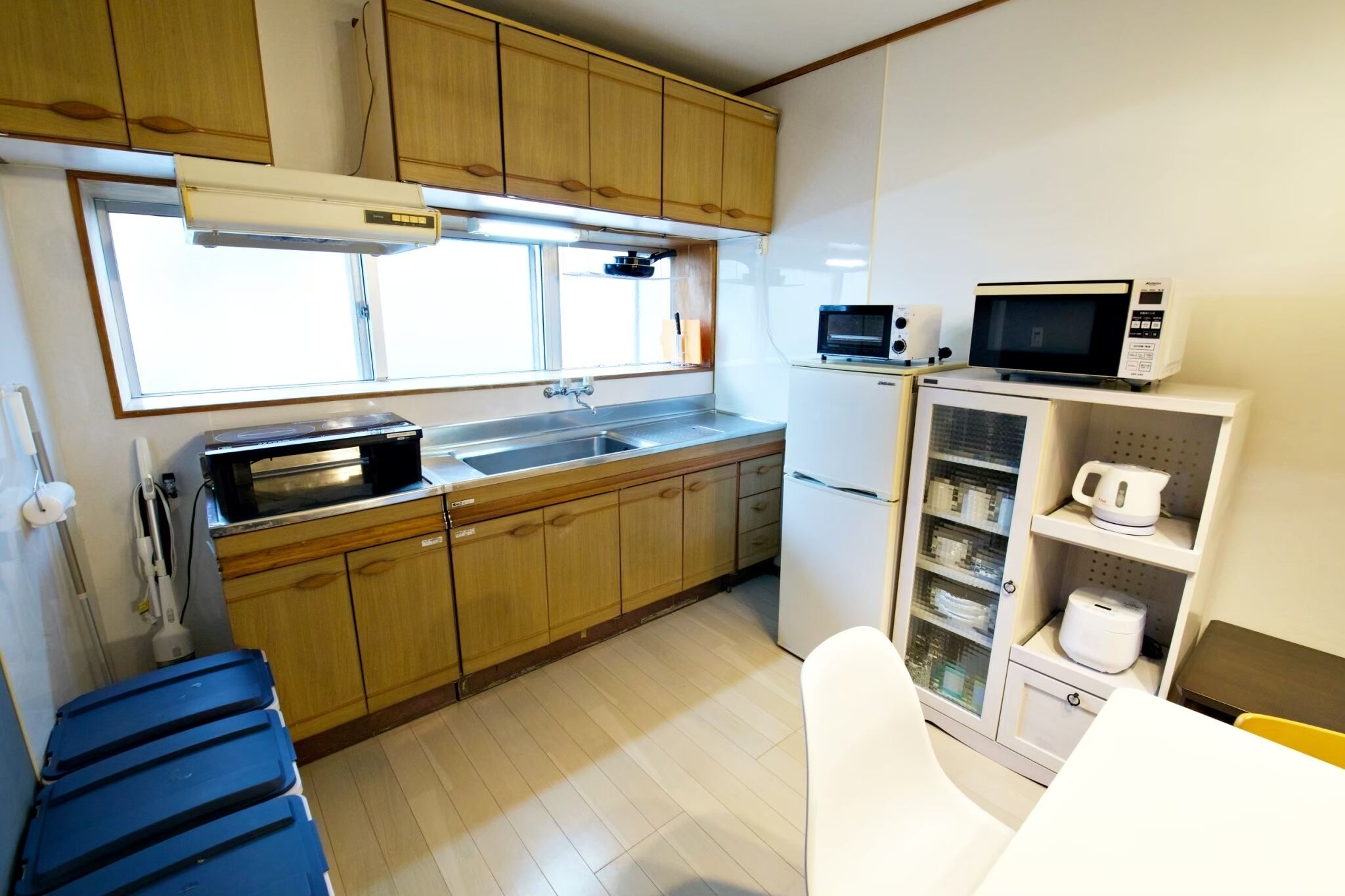 Cocina compacta con armarios de madera, un lavamanos de acero inoxidable, microondas, refrigerador y un pequeño comedor con mesa y sillas.
