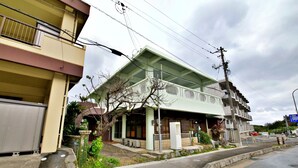 A two-story residential building with a green roof, a balcony on the upper floor, and a small porch area. - Onnason Yamada House (Onna)