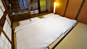 A traditional Japanese-style room with tatami flooring, a futon bed, a shoji screen, and a sliding door. - Onnason Yamada House (Onna)