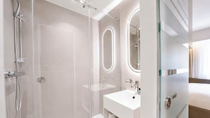 Een moderne badkamer met een douche met glazen wand, een witte wastafel en een spiegel met ronde rand.