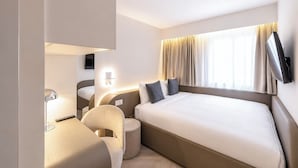 Hotelkamer met een groot bed, een bureau, een stoel, een aan de muur bevestigde televisie en een raam met gordijnen.