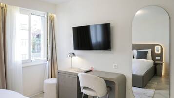 A hotel room with a bed, a desk with a chair, a television, and a large mirror.