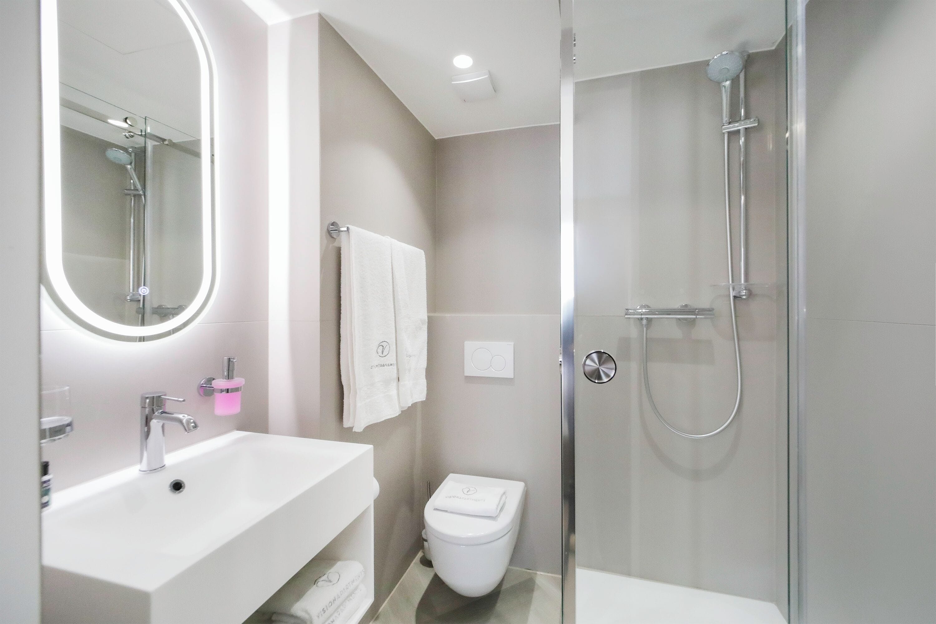 A modern bathroom with a white sink, a glass shower enclosure, and a toilet.