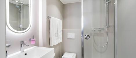 A modern bathroom with a white sink, a glass shower enclosure, and a toilet.