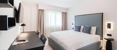 A modern hotel room with a large bed, a desk with a chair, a flat-screen TV, and a small side table.