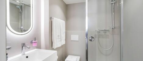Un baño moderno con lavamanos blanco, espejo, inodoro y ducha con mampara de vidrio.