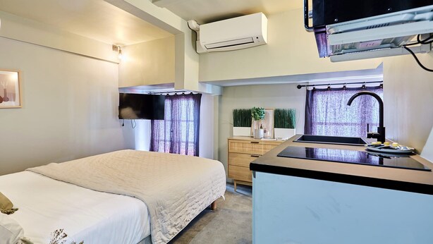 Una habitación de hotel compacta con cama, kitchenette y una ventana pequeña con cortinas.
