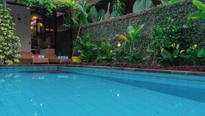Piscina con borde de azulejos, rodeada de exuberante vegetación y una pared cubierta de plantas.