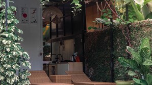 Un espacio lounge moderno al aire libre con mobiliario de mimbre, una piscina pequeña y abundante vegetación.