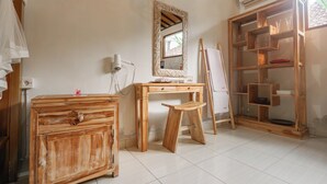Una habitación con un escritorio de madera, un espejo, un armario y una estantería con cristalería.