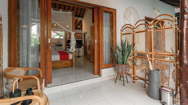 Una habitación con una cama, una silla de mimbre, una planta en maceta y una pantalla de bambú.