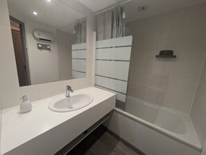 Un baño moderno con lavamanos, espejo y ducha blancos.
