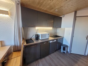 A compact kitchen with dark cabinets, a white microwave, a sink, and a small stool.