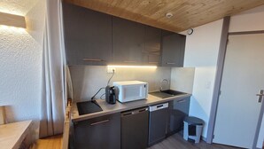 Une cuisine compacte avec des meubles de couleur sombre, un micro-ondes blanc, un évier et un petit tabouret.
