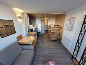 Una habitación compacta con una cama litera de madera, una mesa de comedor con sillas, un sofá y una kitchenette al fondo.