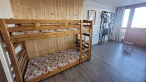 Un lit superposé avec un matelas à motifs, dans une pièce au plancher en bois et au plafond en pente.