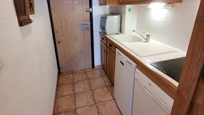 Een kleine keuken met houten kastjes, een wit aanrechtblad, een ingebouwde vaatwasser en een klein spoelbakje.