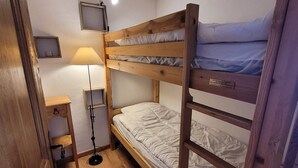 Een slaapkamer met stapelbed, een bedlampje, een klein tafeltje en een televisie aan de muur.