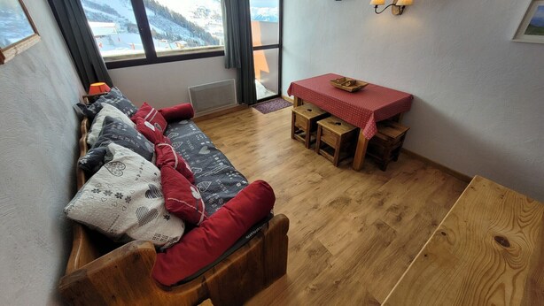 Een gezellige kamer met een houten bank, een kleine eettafel en een aan de muur bevestigde televisie.